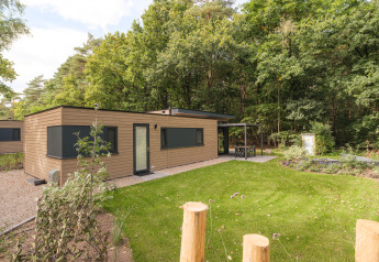 Lodge Cannenburch Deluxe en Veluwepark de Bosgraaf, Países Bajos, con patio y jardín verde al fondo.