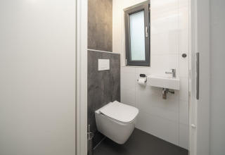 Moderne compacte badkamer met hangtoilet, kleine wastafel en raam in Cannenburch Deluxe op Veluwepark de Bosgraaf.