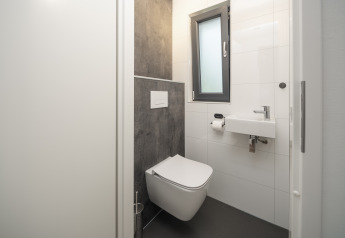 Salle de bain moderne et compacte avec WC suspendu, petit lavabo et fenêtre au lodge Cannenburch Deluxe.