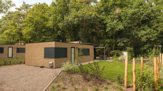 Vue extérieure du lodge Cannenburch Deluxe au Veluwepark de Bosgraaf, entouré de forêt verdoyante.