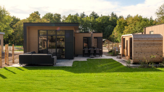 Außenansicht der Essenburgh-Lodge mit Whirlpool, Sauna, grüner Rasenfläche und moderner Terrasse.