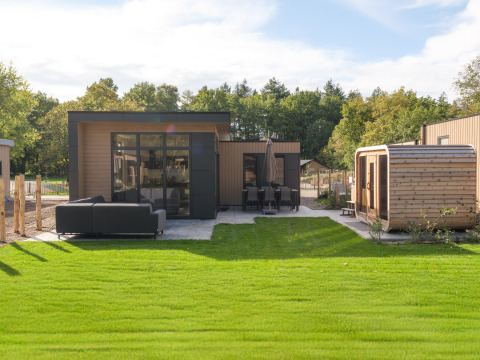 Außenansicht der Essenburgh-Lodge mit Whirlpool, Sauna, grüner Rasenfläche und moderner Terrasse.