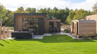 Buitenaanzicht van Essenburgh lodge met hot tub en sauna, tuinset, eettafel en groene grasmat.