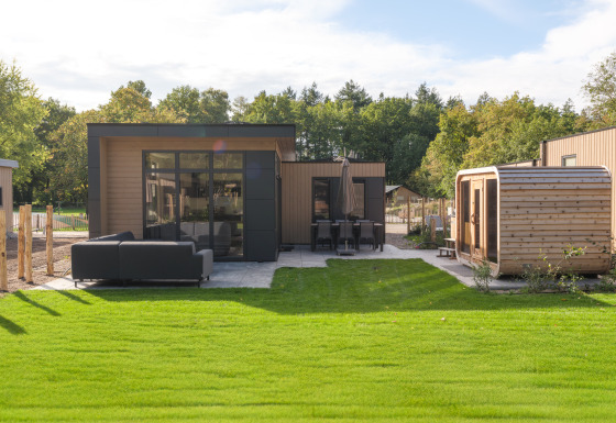 Vista exterior del lodge Essenburgh con jacuzzi y sauna, zona de césped, asientos y comedor al aire libre.