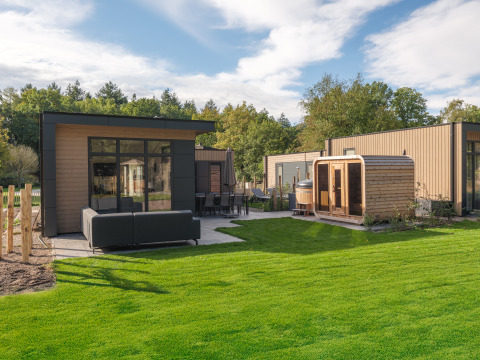 Moderne lodge Essenburgh med spabad og sauna i Veluwepark de Bosgraaf, Holland, omgivet af grønt.