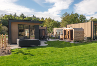 Moderne lodge Essenburgh med spabad og sauna i Veluwepark de Bosgraaf, Holland, omgivet af grønt.