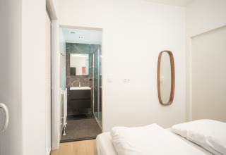 Camera da letto con bagno moderno, specchio a parete e biancheria bianca nella lodge Essenburgh al Veluwepark de Bosgraaf.