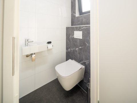 Baño moderno con inodoro suspendido y lavabo pequeño, Essenburgh Lodge, Veluwepark de Bosgraaf, Países Bajos.