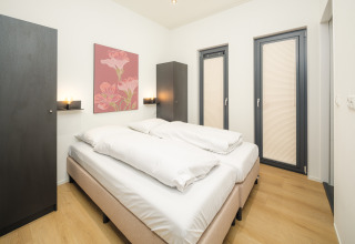 Modern bedroom at Essenburgh Lodge featuring a double bed, soft lighting, and minimalist decor in Veluwepark de Bosgraaf, Netherlands.