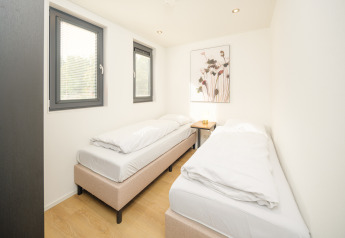 Chambre lumineuse avec deux lits simples, grandes fenêtres et décoration minimaliste au lodge Essenburgh.