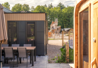 Moderne Lodge mit Terrasse, Esstisch, Whirlpool und Sauna, mit Spielplatz im Hintergrund im Veluwepark de Bosgraaf.