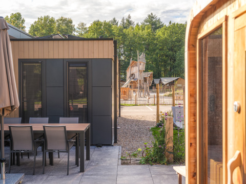 Modern lodge with patio, dining table, hot tub, and sauna, overlooking playground at Veluwepark de Bosgraaf.