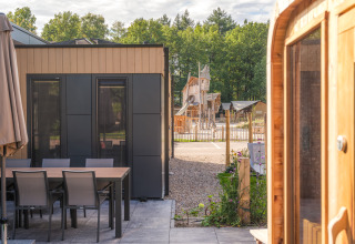 Moderne lodge med terrasse, spisebord, spabad og sauna, med legeplads i baggrunden i Veluwepark de Bosgraaf.