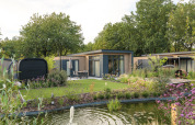 Lodge moderno Essenburgh Comfort con jacuzzi y sauna en Veluwepark de Bosgraaf, rodeado de jardines verdes.