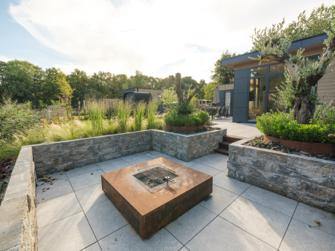 Modern outdoor lounge with firepit and Essenburgh Comfort lodge at Veluwepark de Bosgraaf in the Netherlands.