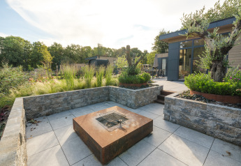 Zona de estar exterior moderna con fogata y lodge Essenburgh Comfort en Veluwepark de Bosgraaf, Países Bajos.