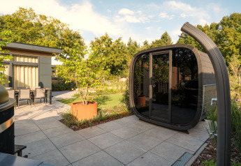 Moderne udendørs lodge med glasdøre, træer og havemøbler på Essenburgh Comfort met Hottub & Sauna i Veluwepark de Bosgraaf.