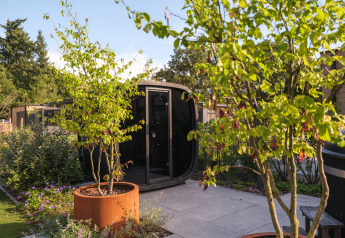 Moderne lodge met zwarte sauna en hottub in een groene tuin bij Veluwepark de Bosgraaf, Nederland.