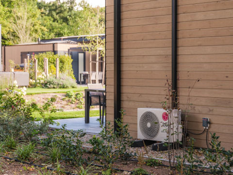 Außenbereich einer Lodge im Veluwepark de Bosgraaf mit Terrasse, Pflanzen und Klimaanlage.