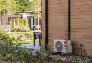 Außenbereich einer Lodge im Veluwepark de Bosgraaf mit Terrasse, Pflanzen und Klimaanlage.
