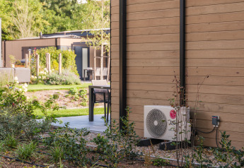 Außenbereich einer Lodge im Veluwepark de Bosgraaf mit Terrasse, Pflanzen und Klimaanlage.