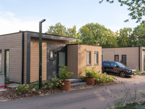 Moderne Ferienlodge im Veluwepark de Bosgraaf, Niederlande, mit Holzverkleidung und geparktem Auto.