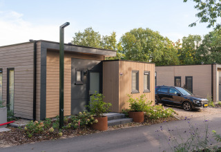Moderne Ferienlodge im Veluwepark de Bosgraaf, Niederlande, mit Holzverkleidung und geparktem Auto.