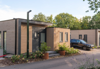 Moderne Ferienlodge im Veluwepark de Bosgraaf, Niederlande, mit Holzverkleidung und geparktem Auto.