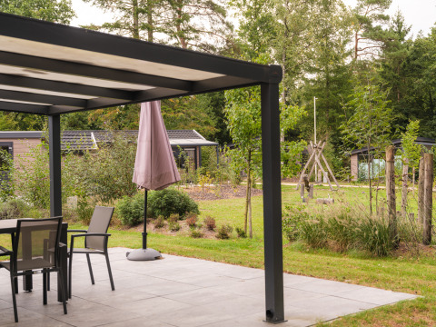 Terrasse moderne d’un lodge avec mobilier de jardin, parasol et vue sur un espace vert et des arbres.