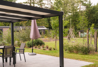 Terrasse moderne d’un lodge avec mobilier de jardin, parasol et vue sur un espace vert et des arbres.