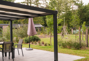 Moderne Terrasse am Lodge mit Gartenmöbeln, Sonnenschirm und Blick auf grüne Natur und Bäume.