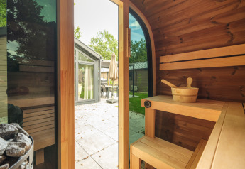 Vista dall'interno di una sauna in legno con porta aperta sulla terrazza al Doornenburg Lodge Comfort nei Paesi Bassi.