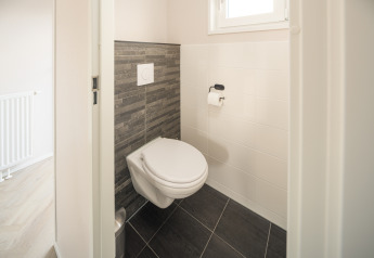 Baño moderno con inodoro de pared y azulejos oscuros en Doornenburg Lodge Comfort, Países Bajos.