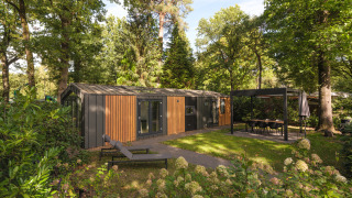 Lodge Cozy Chalet moderne entouré d’arbres, avec transat et coin repas couvert, en pleine verdure.