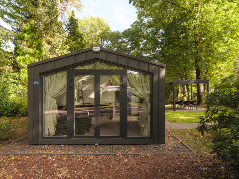 Modernes Chalet mit Glasfront und Vorhängen im Grünen im Veluwepark de Bosgraaf, Niederlande.