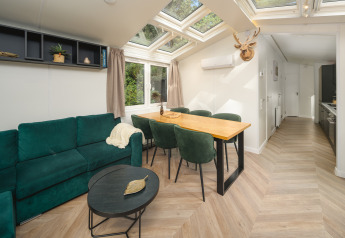 Salon moderne et lumineux au Cozy Chalet de Veluwepark de Bosgraaf, canapé vert et table à manger.