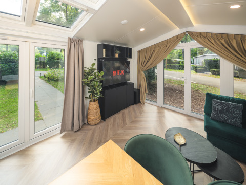 Moderne stue i Cozy Chalet på Veluwepark de Bosgraaf, Holland, med store vinduer og grøn udsigt.