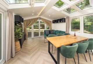 Modernes Chalet mit großem Esstisch, grünen Stühlen und Panoramafenstern im Veluwepark de Bosgraaf, Niederlande.