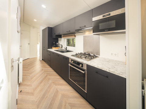 Cucina moderna con mobili neri e piano in marmo al Cozy Chalet nel Veluwepark de Bosgraaf, Paesi Bassi.