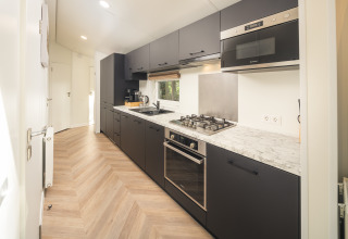 Cucina moderna con mobili neri e piano in marmo al Cozy Chalet nel Veluwepark de Bosgraaf, Paesi Bassi.