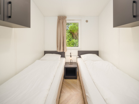 Et lyst og simpelt soveværelse med to enkeltsenge på Cozy Chalet ved Veluwepark de Bosgraaf i Nederlandene.