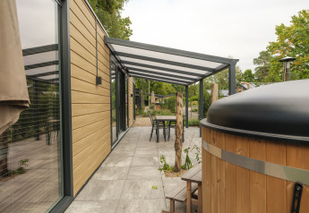 Terraza exterior en la cabaña Rosendael Comfort con asientos cubiertos y jacuzzi en Veluwepark de Bosgraaf.