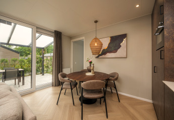 Spisestue i Rosendael Comfort-lodge med rundt bord, fire stole og stor glasdør til terrasse i Veluwepark de Bosgraaf.