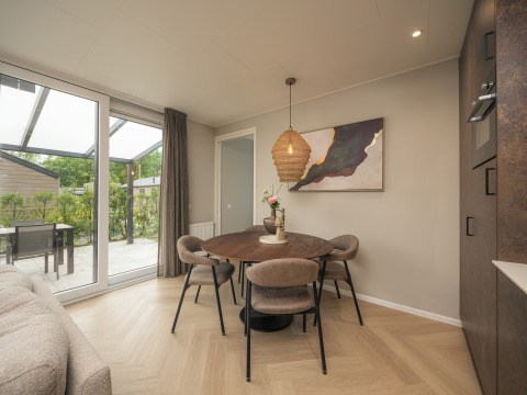 Eethoek in Rosendael Comfort-lodge met ronde tafel, vier stoelen en schuifraam in Veluwepark de Bosgraaf.