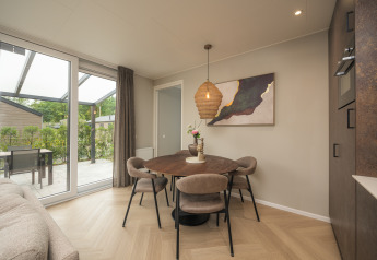 Spisestue i Rosendael Comfort-lodge med rundt bord, fire stole og stor glasdør til terrasse i Veluwepark de Bosgraaf.