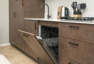 Cucina moderna con lavastoviglie a incasso aperta, fornelli e utensili al lodge Rosendael Comfort nei Paesi Bassi.
