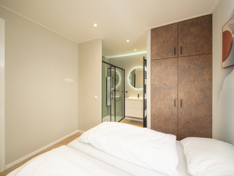 Modernes Schlafzimmer mit Doppelbett, Kleiderschrank und eigenem Bad in der Rosendael Comfort Lodge im Veluwepark de Bosgraaf.