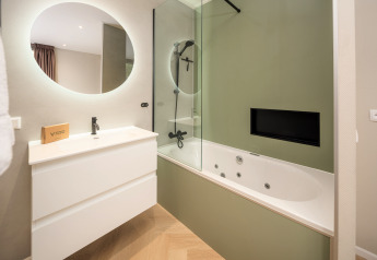 Baño moderno con espejo redondo, lavabo blanco y bañera de hidromasaje en Rosendael Comfort, Veluwepark de Bosgraaf, Países Bajos.