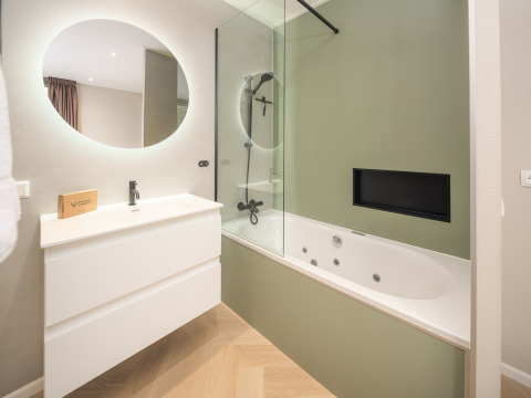 Baño moderno con espejo redondo, lavabo blanco y bañera de hidromasaje en Rosendael Comfort, Veluwepark de Bosgraaf, Países Bajos.
