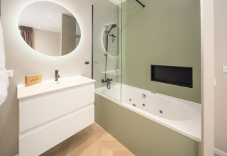 Baño moderno con espejo redondo, lavabo blanco y bañera de hidromasaje en Rosendael Comfort, Veluwepark de Bosgraaf, Países Bajos.